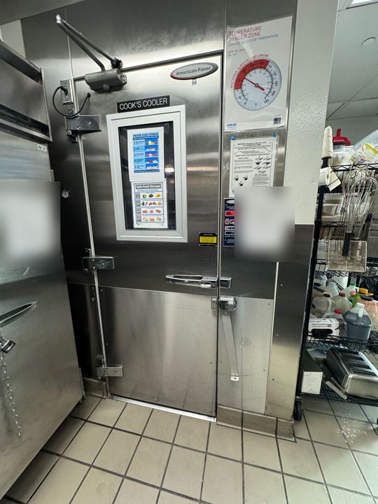Stainless American Panel walk-in cooler door labeled Cook's Cooler in a restaurant kitchen, logs blurred