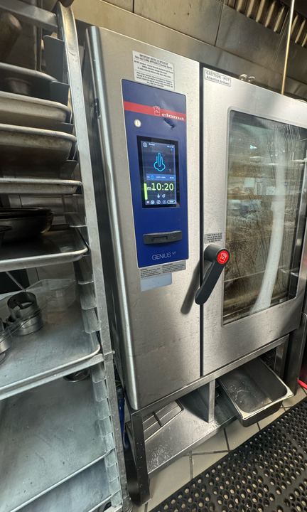 Stainless Eloma Genius MT combi oven on a stand next to a sheet pan rack in a restaurant kitchen