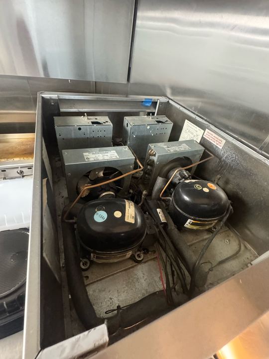 Two compressors with their electrical boxes in the machine compartment of a commercial refrigeration unit
