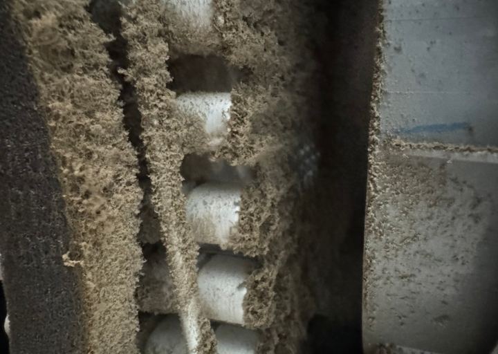 Close-up of a refrigerator condenser coil with the fins fully covered by a thick layer of dust