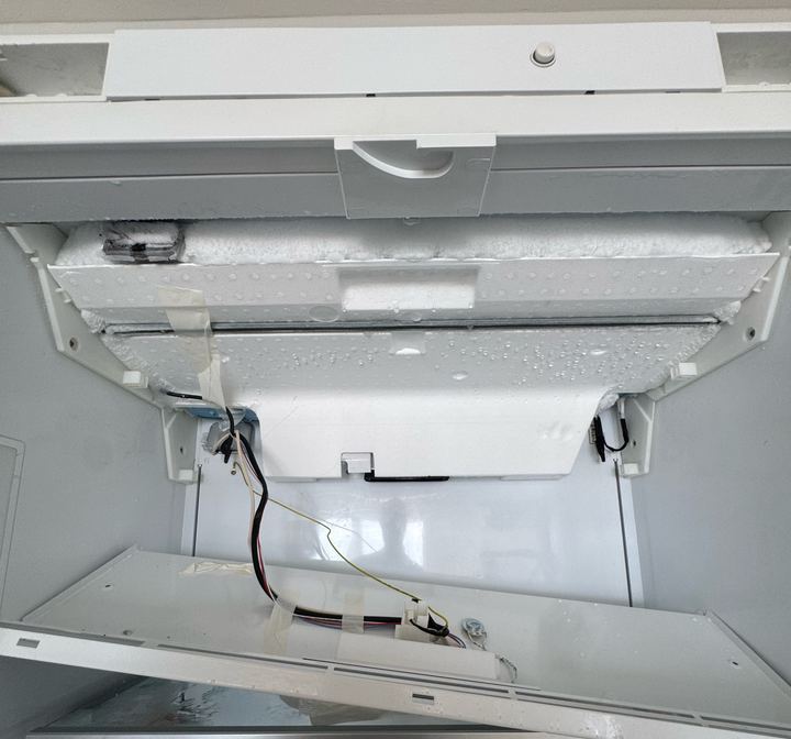 Built-in refrigerator with the evaporator cover lowered, showing ice built up across the evaporator area