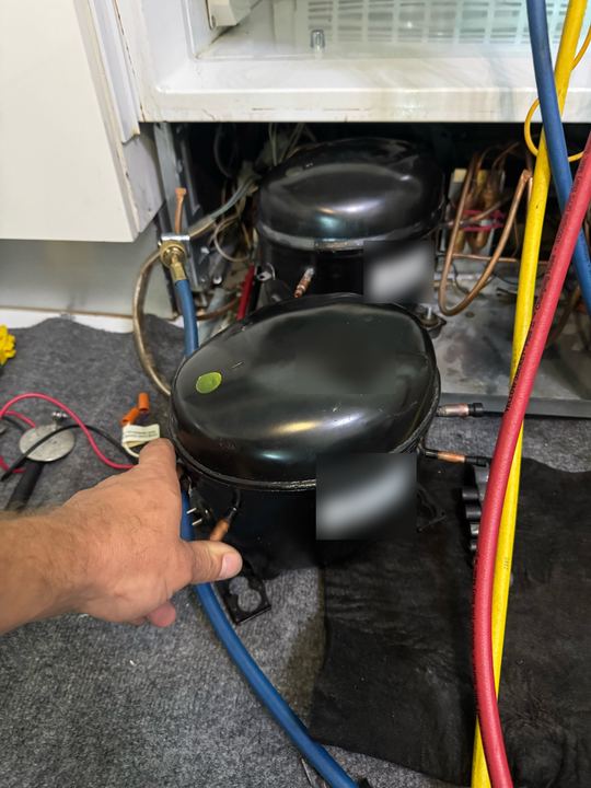 Technician's hand on a compressor next to a second compressor in the machine compartment