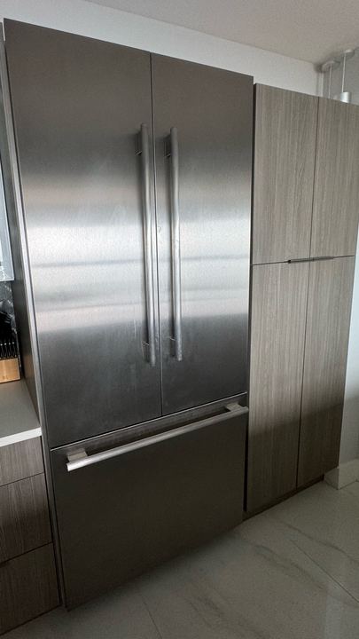 Stainless French-door built-in refrigerator between modern wood-grain cabinets