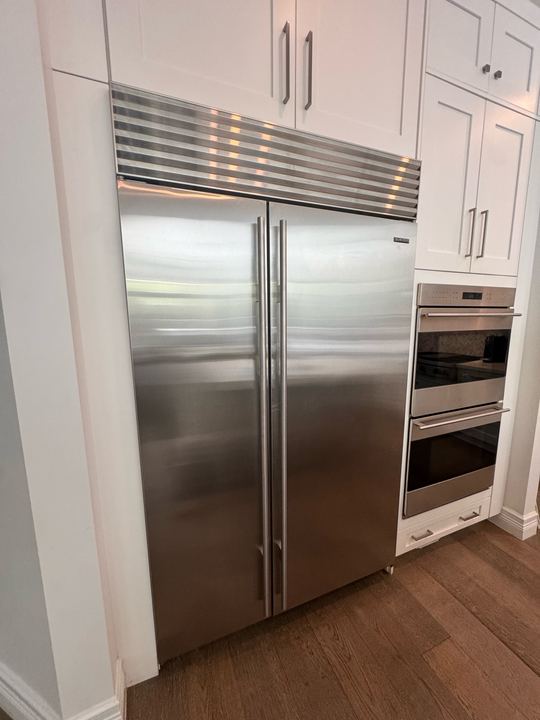 Stainless Sub-Zero built-in side-by-side refrigerator with grille, next to a Wolf double wall oven in white cabinetry