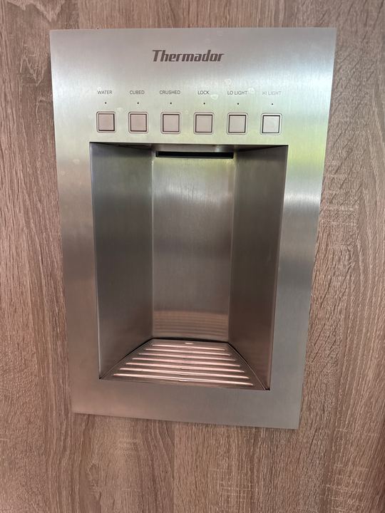 Stainless Thermador water and ice dispenser set into a wood-grain panel-ready refrigerator door