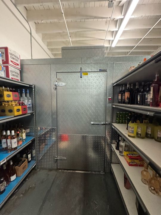 Stainless walk-in cooler box with a diamond-plate door between store shelves