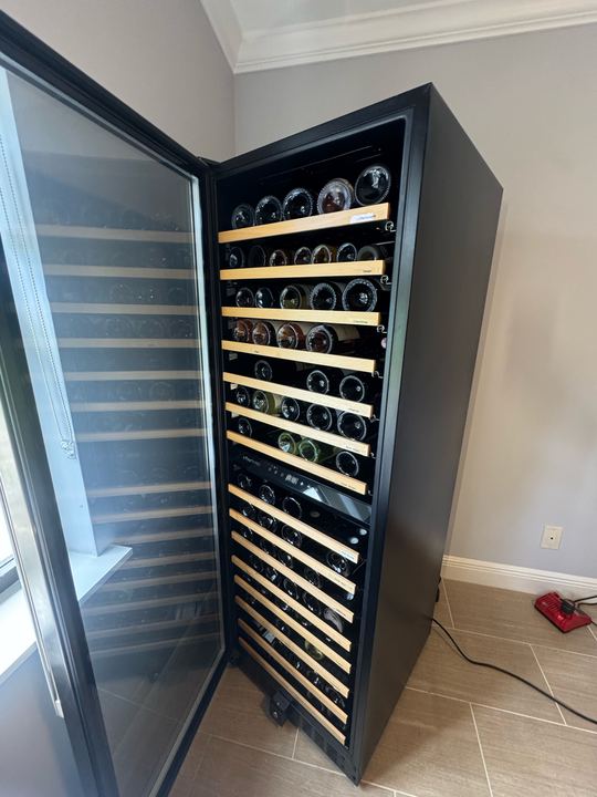 Open full-height wine cooler with wood-front shelves loaded with wine bottles